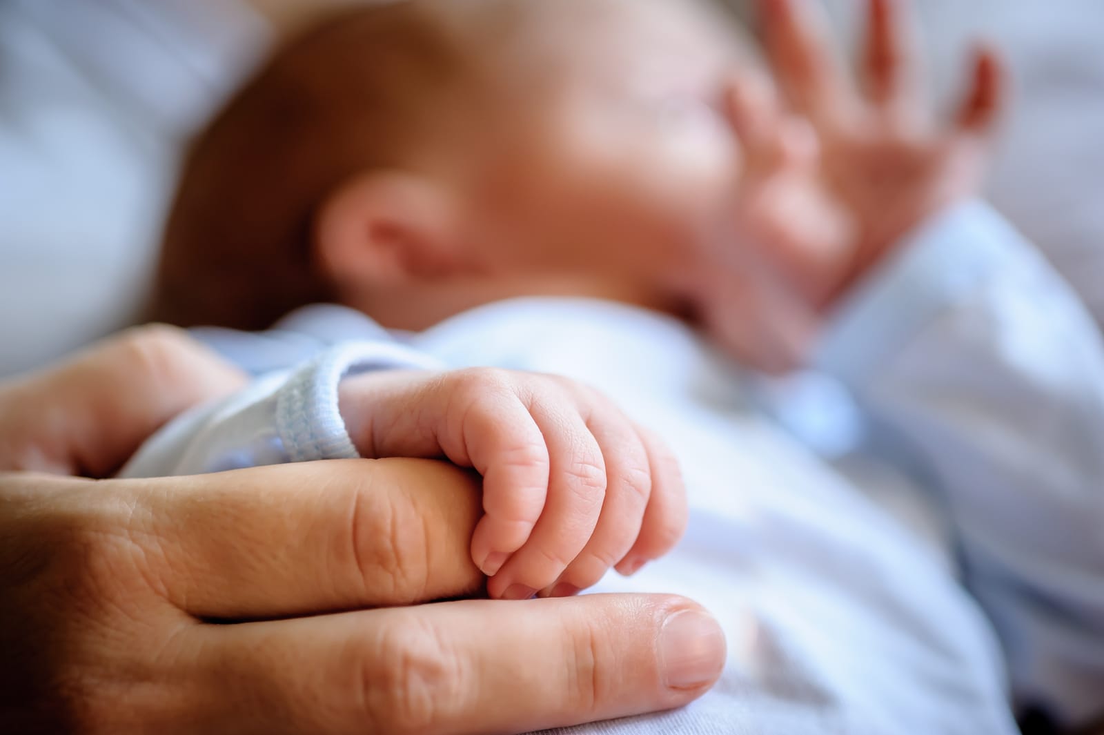 Die Hand eines Babys umschließt den Finger eines Elternteils